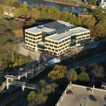 The College of Public Health Building (CPHB), seen looking toward the northeast. In the lower right is the Newton Road Ramp, and in the lower left is the pedestrian bridge that connects the ramp to CPHB over Highway 6 / 2nd Street. The Iowa River is at the top.