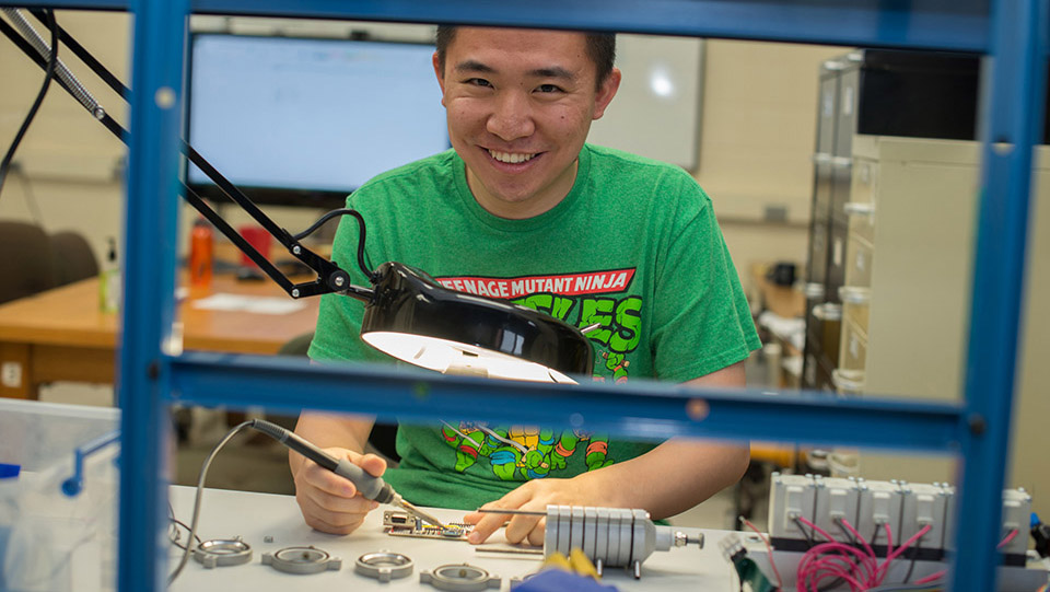 Photo of a student with a soldering iron working in a lab