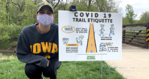 Portrait of Anne Abbott with one of her COVID-19 trail etiquette signs