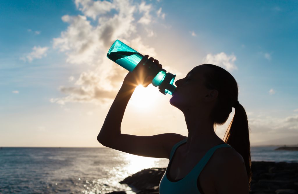 Young woman drinking from water bottle on beach