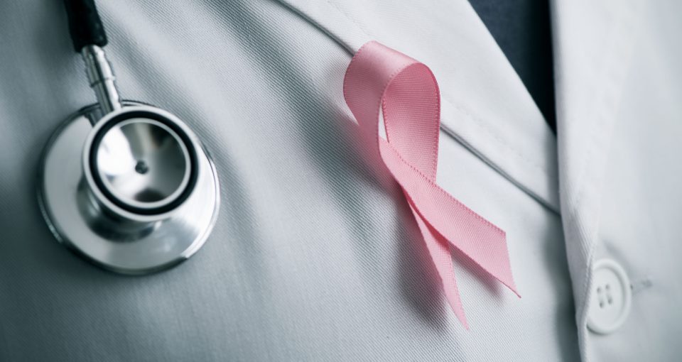 closeup of a young caucasian doctor man with a pink ribbon for the breast cancer awareness pinned in the flap of his white coat