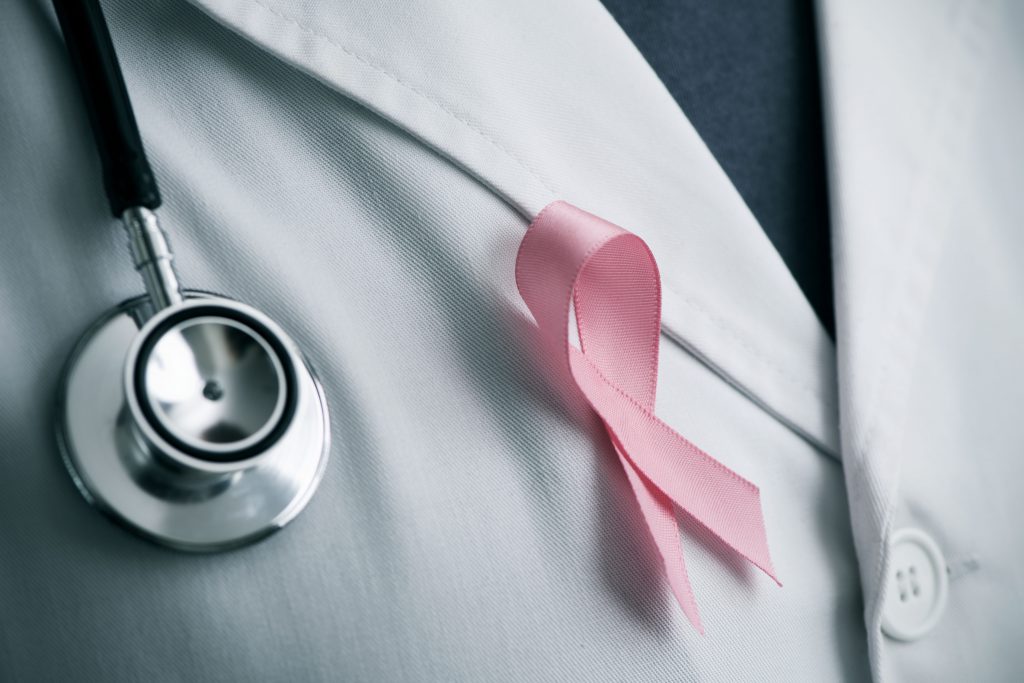 closeup of a young caucasian doctor man with a pink ribbon for the breast cancer awareness pinned in the flap of his white coat