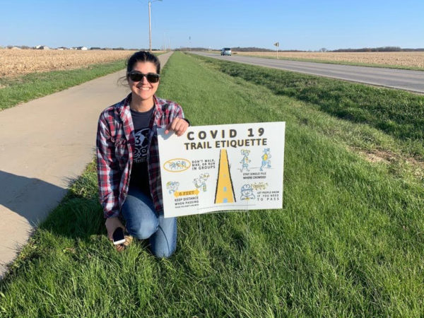 Anne Abbott poses along a trail with a social distancing sign