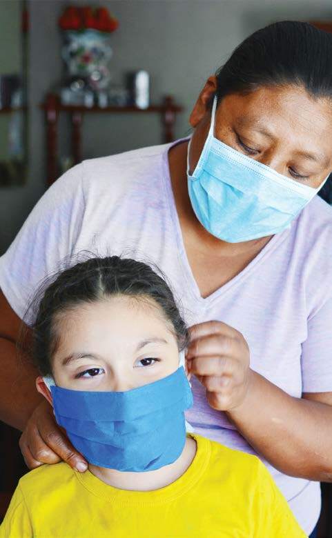 a woman helps put a face mask on a young girl