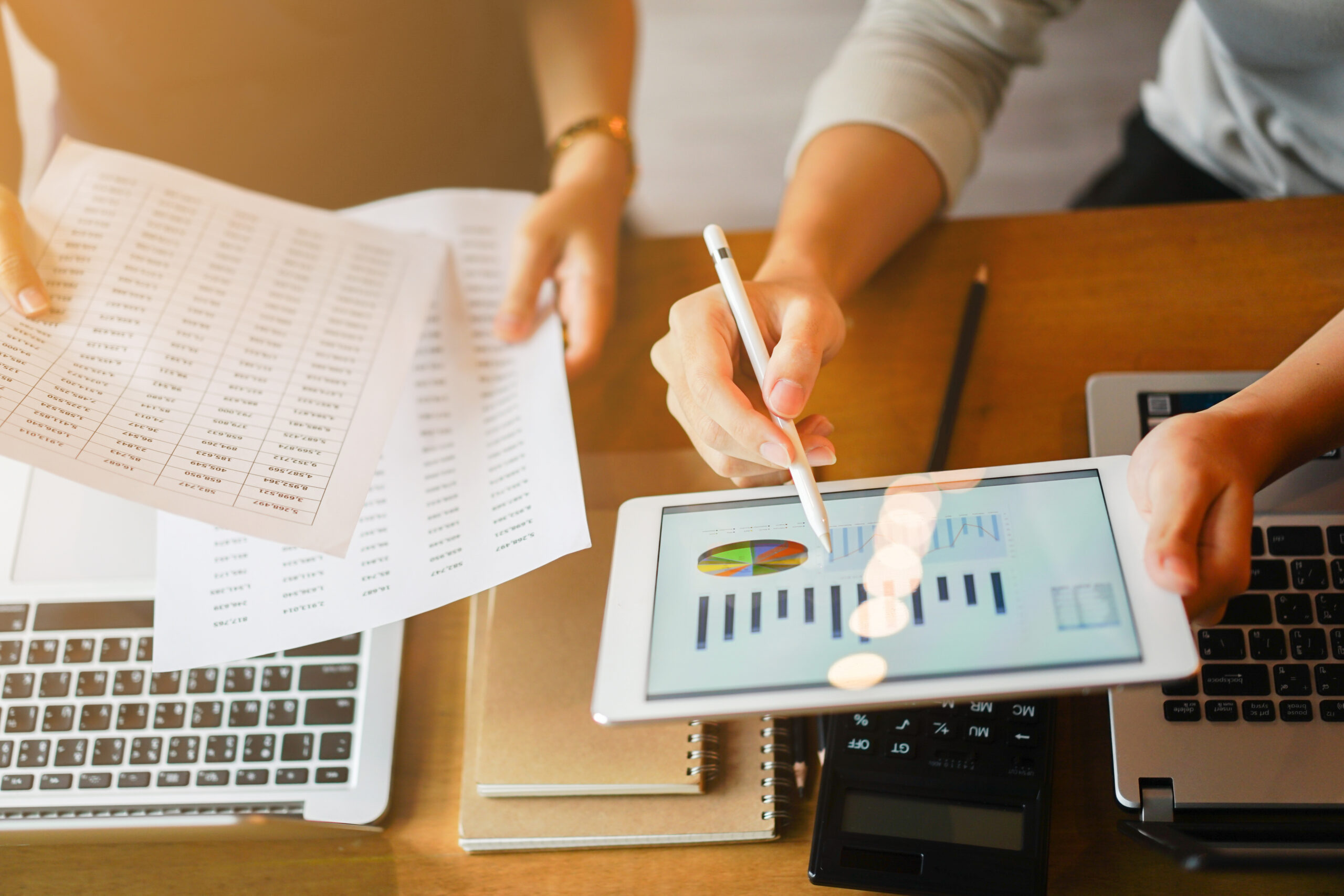 Data analysts comparing data on a tablet and on printed pages.