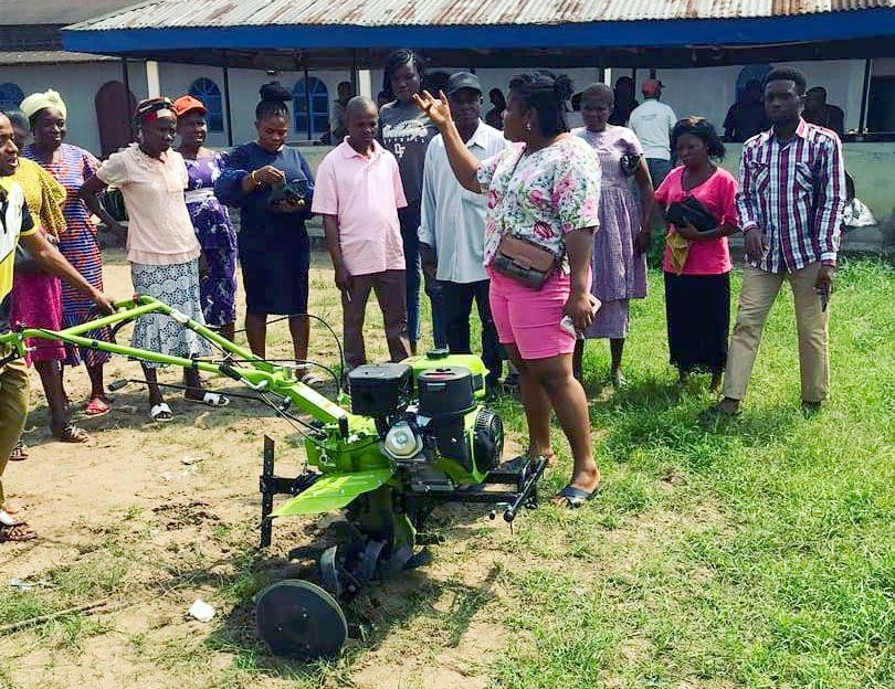 A group of farmers listen to a demonstration of a green power tiller