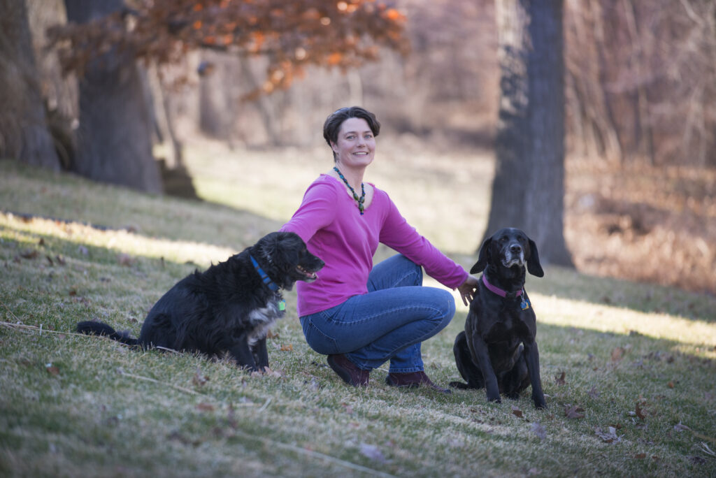 Christine Petersen poses outside with two black dogs 