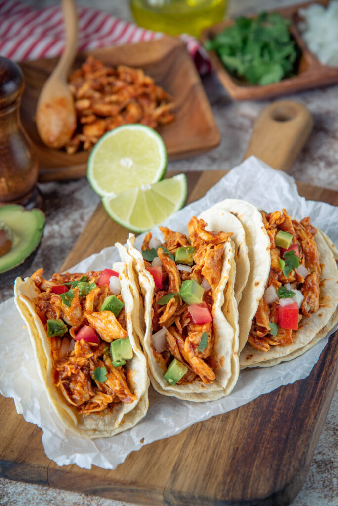 photo of three tacos filled with chicken, avocado, and tomato