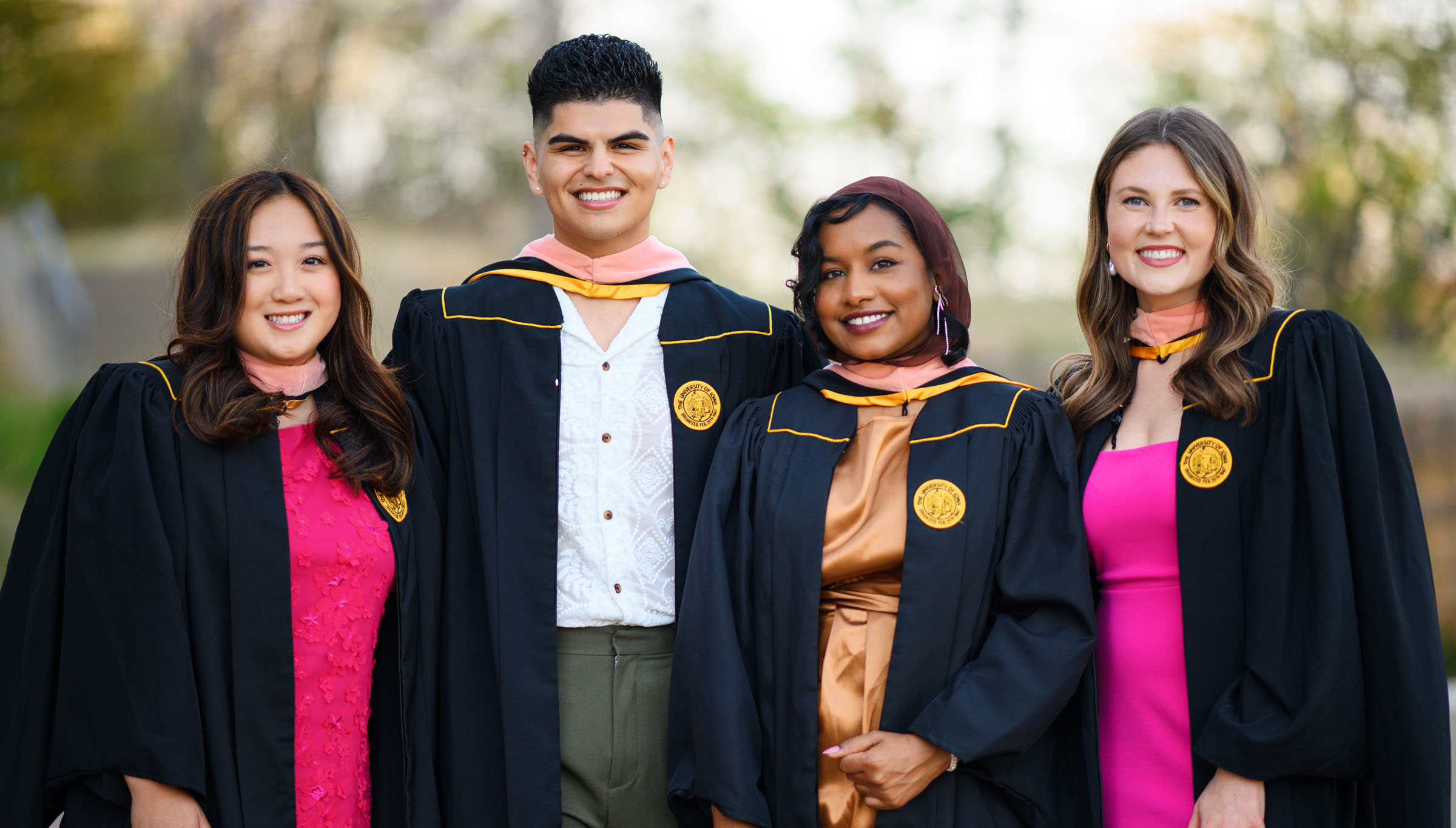 Bonnie Gao, Eric Ramos, Assjad Haj, and Olivia Wilson pose in their graduation regalia on the Pentacrest in Iowa City in 2023.