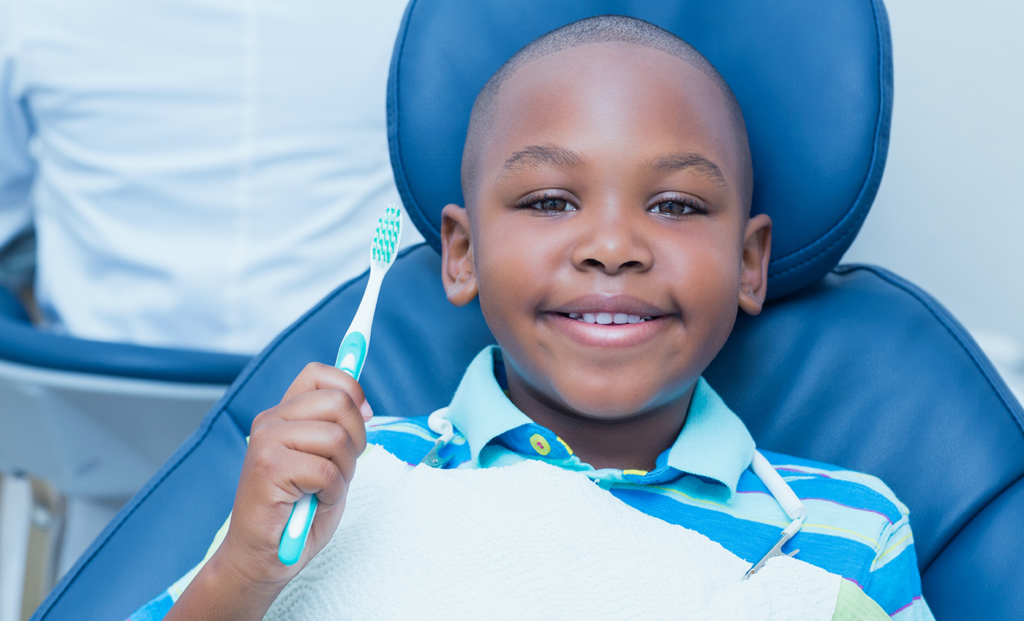 a young boy smiling and holding a toothbrush while seated in a dental chair