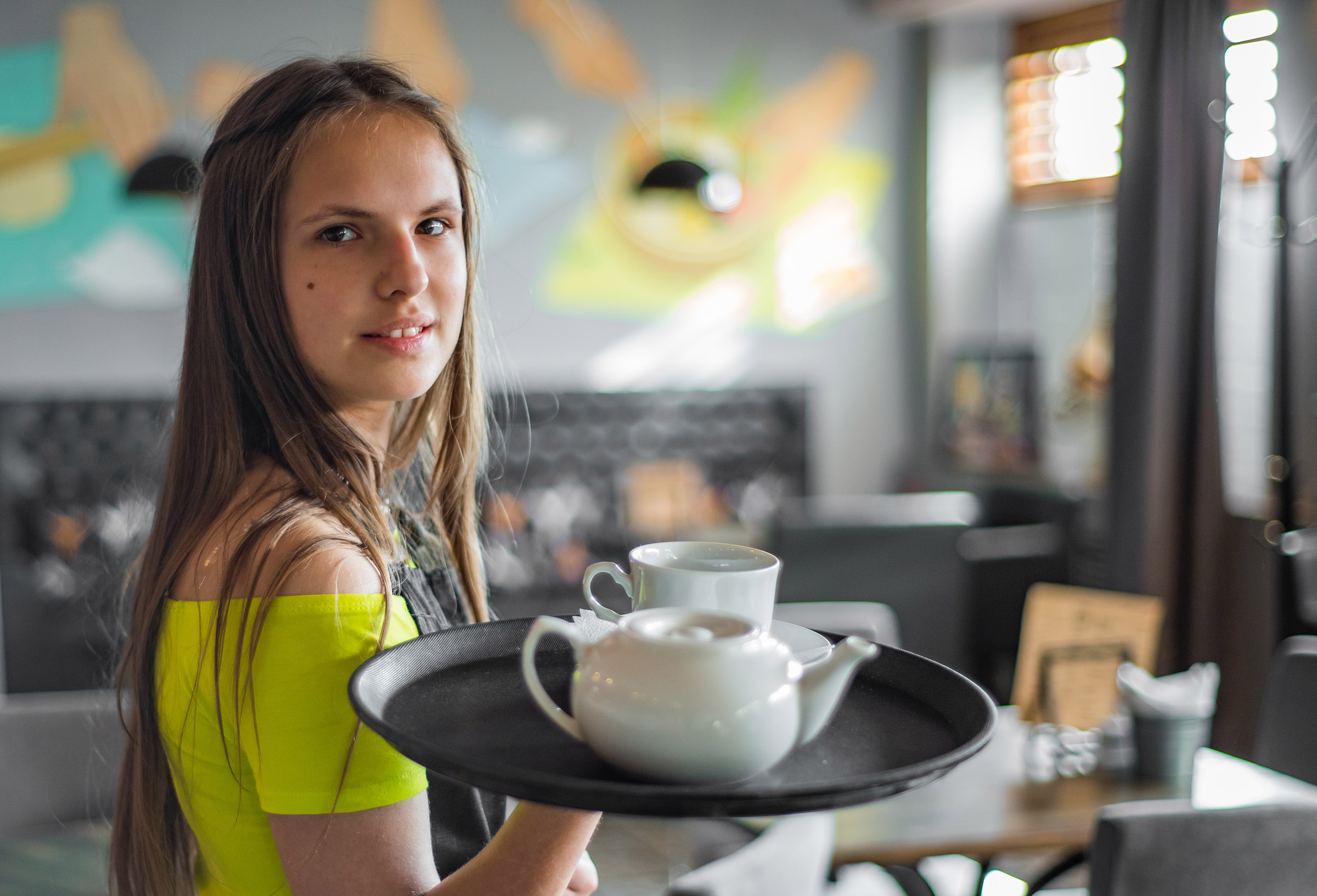 A teen girl serves coffee at a restaurant.