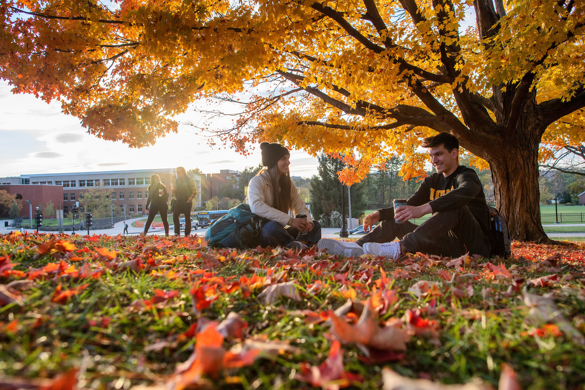 Two students sit on the Old Capitol lawn amidst fallen leaves.