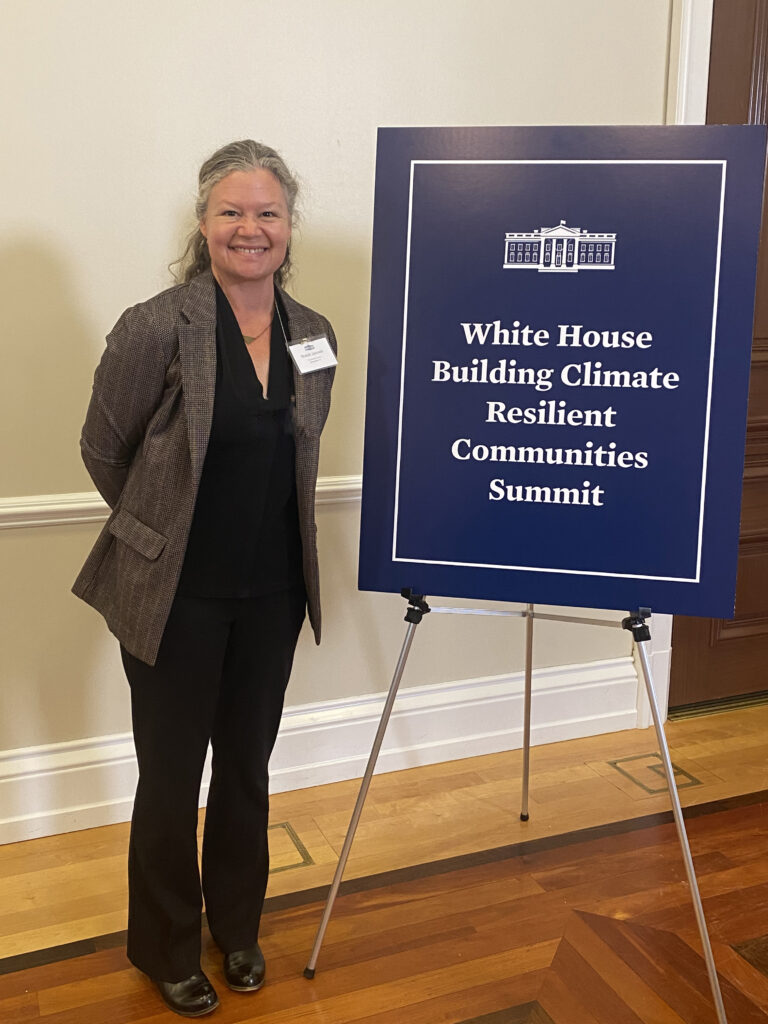 Brandi Janssen stands in front of a sign for the White House Summit on Building Climate Resilient Communities