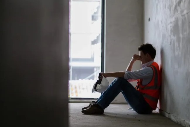 Distraught construction worker seated and leaning against a wall