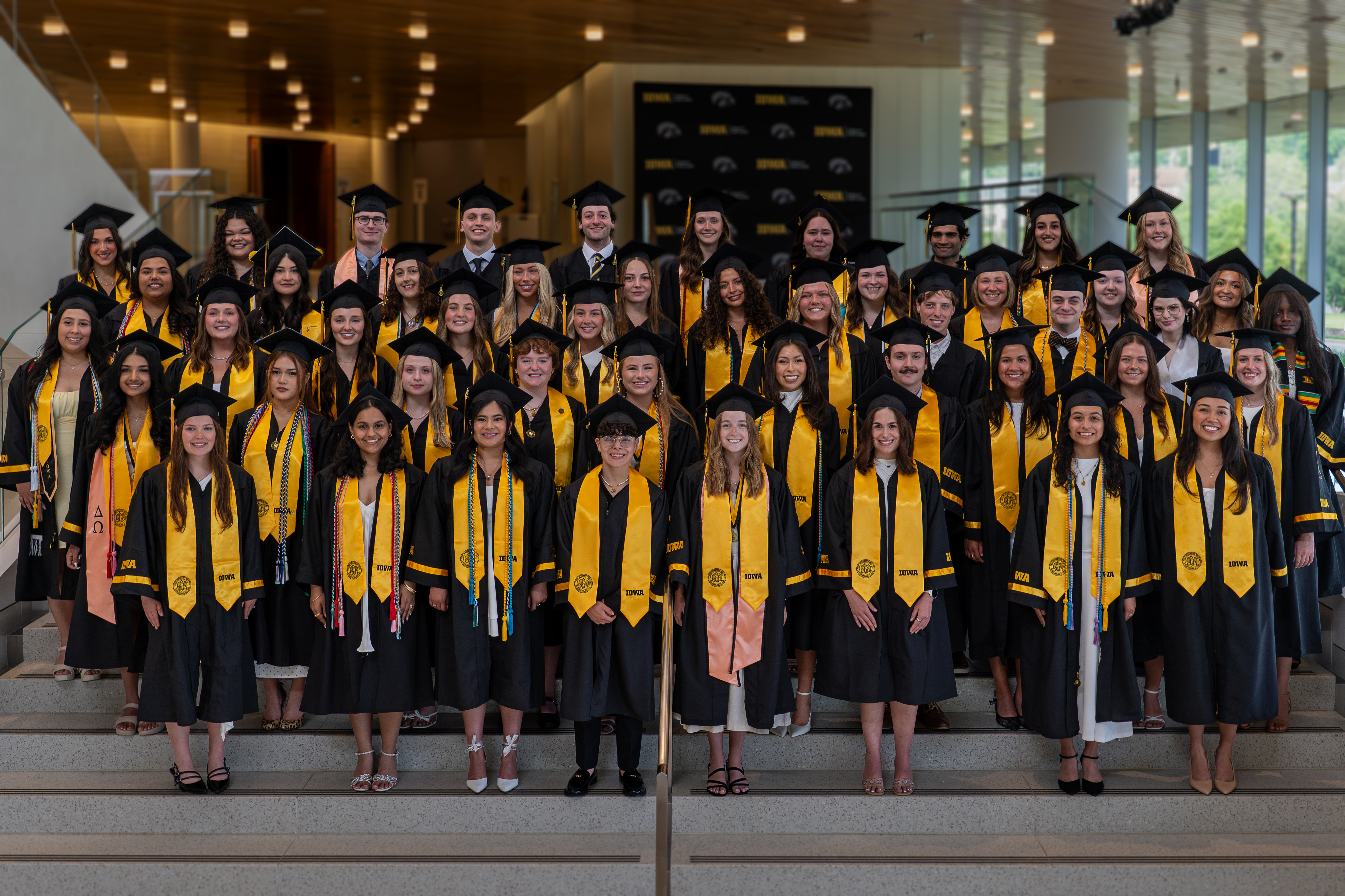 The class of 2026 of the College of Public Health pose on the steps inside Hancher Auditorium at commencement.